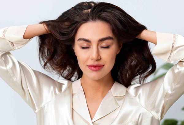 A imagem mostra uma mulher com uma expressão relaxada enquanto está com as duas mãos na cabeça.